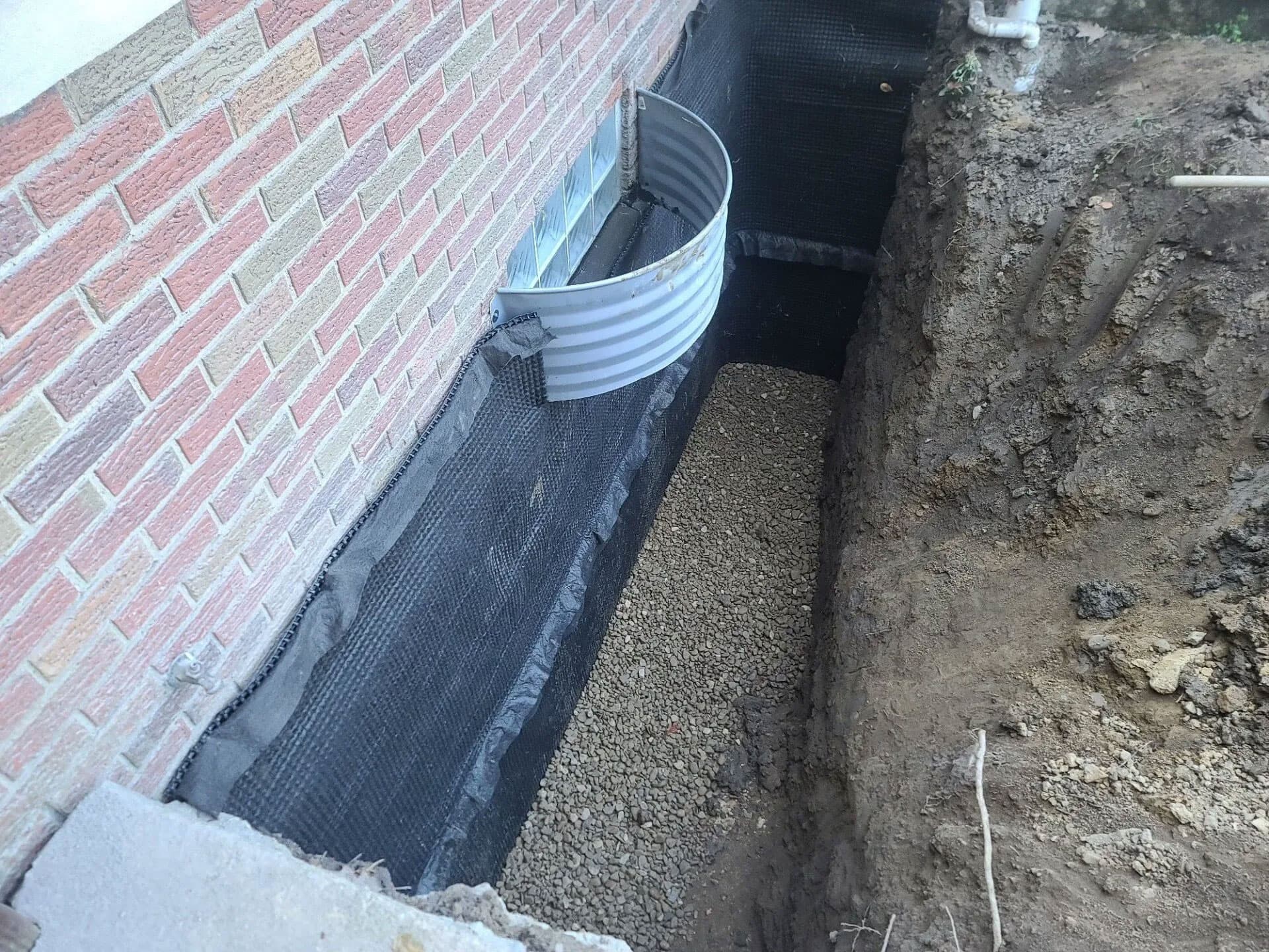 Exterior excavation down to basement footer showing window well and dimpled drainage membrane