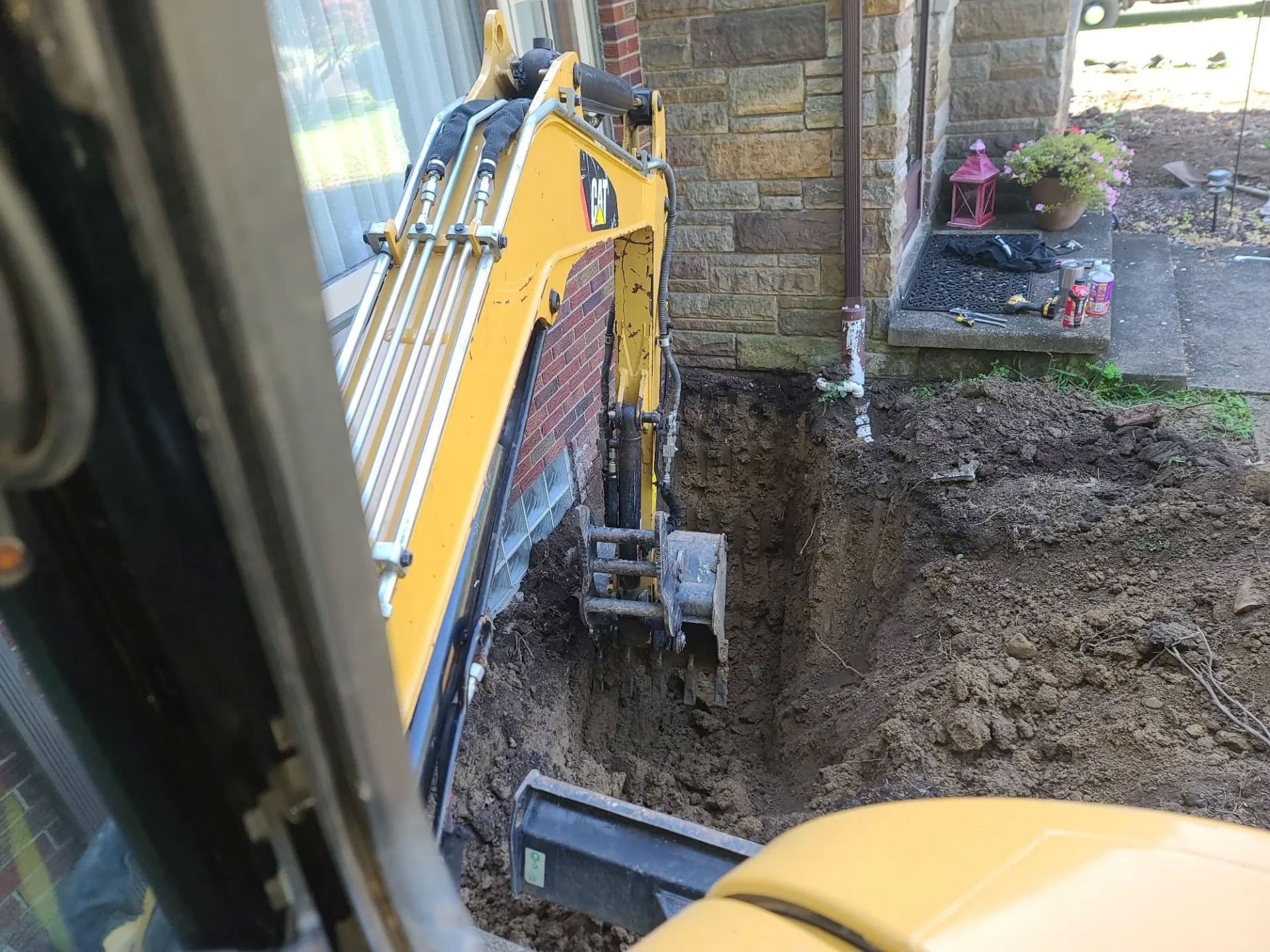 CAT mini excavator digging next to a stone-faced home foundation for foundation repair