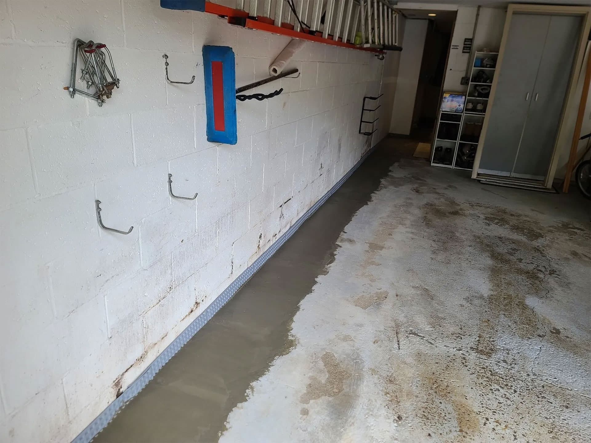 Fresh concrete sub-floor drainage channel along a cinder-block basement wall in a Western PA home