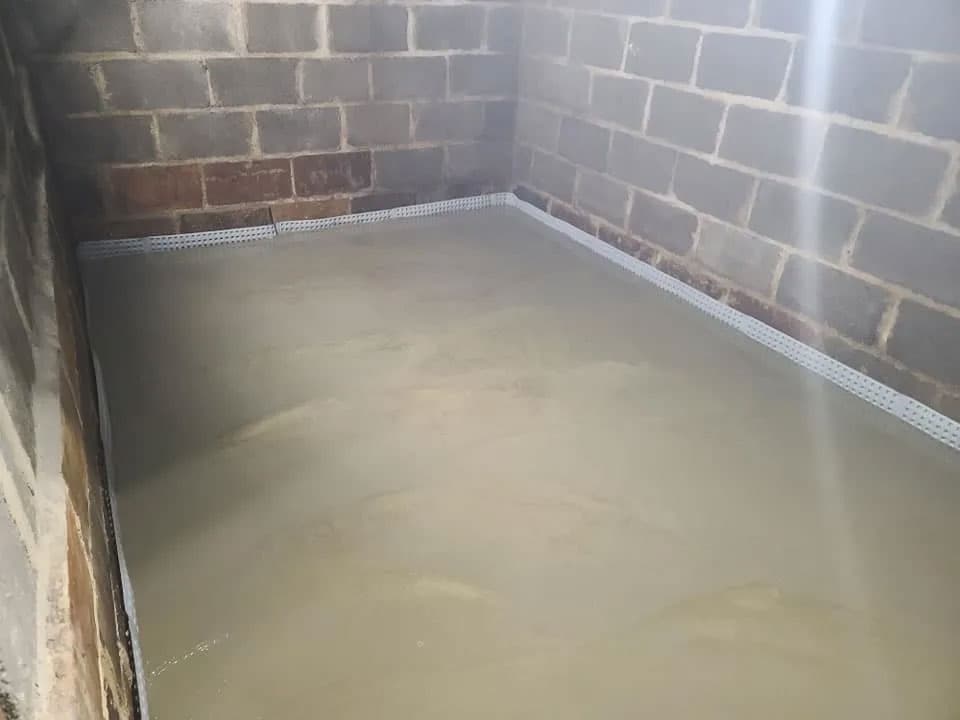 Completed interior basement drainage system with dimpled wall membrane and fresh concrete floor