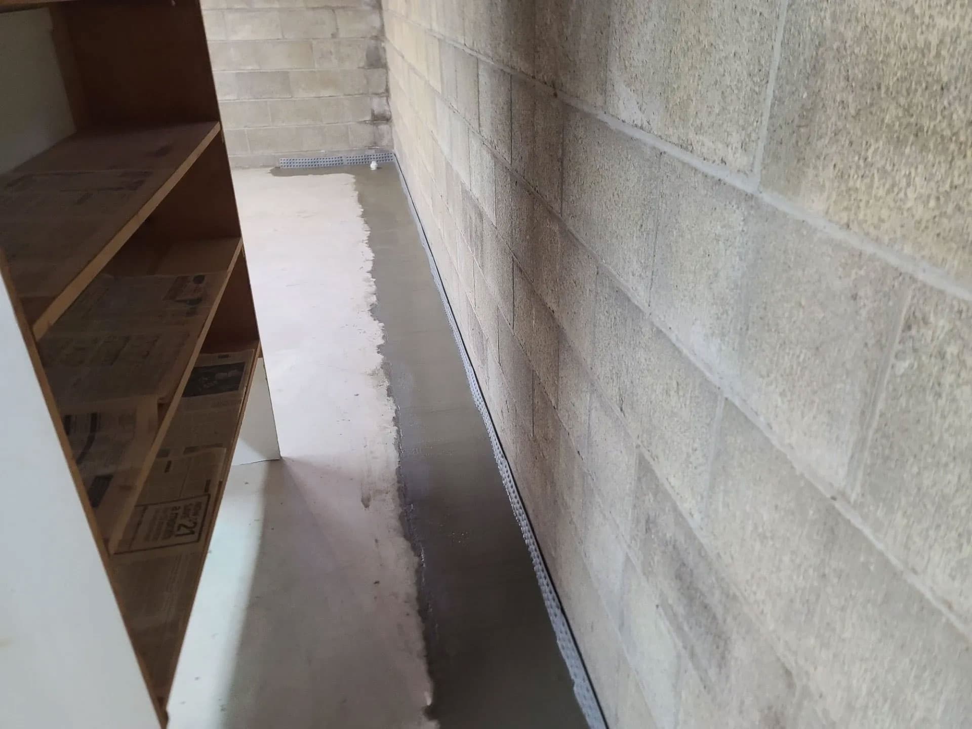 Sub-floor drainage channel installed along a cinder-block wall in a Mercer County basement