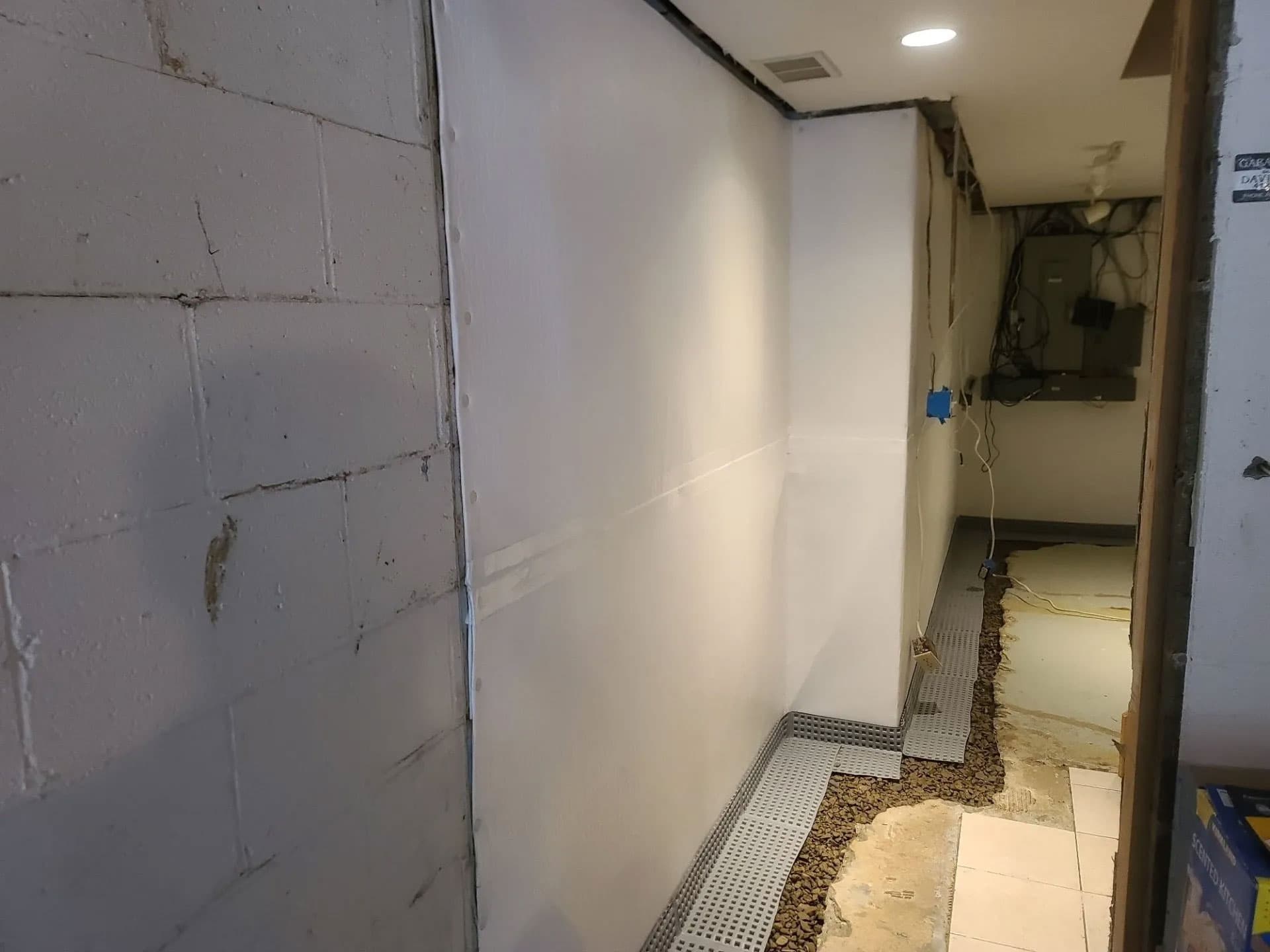 Basement wall with white vapor barrier panel and dimpled sub-floor drainage membrane exposed