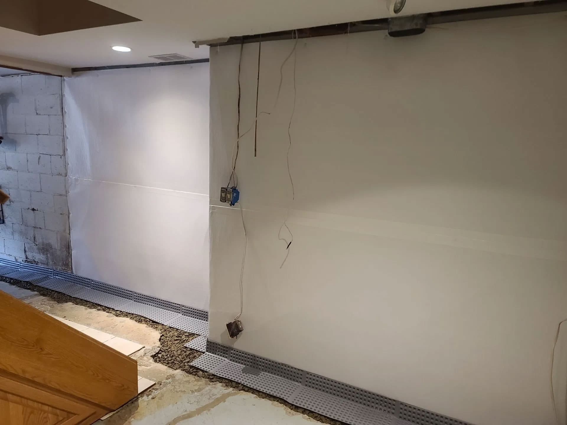 Large basement room with floor-to-ceiling white vapor barrier on walls and perimeter drainage
